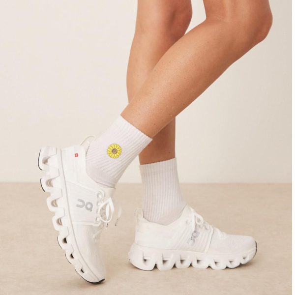 White chunky sneakers worn with white socks featuring a small yellow sunflower design, shown from the side for a fashion/product shot.