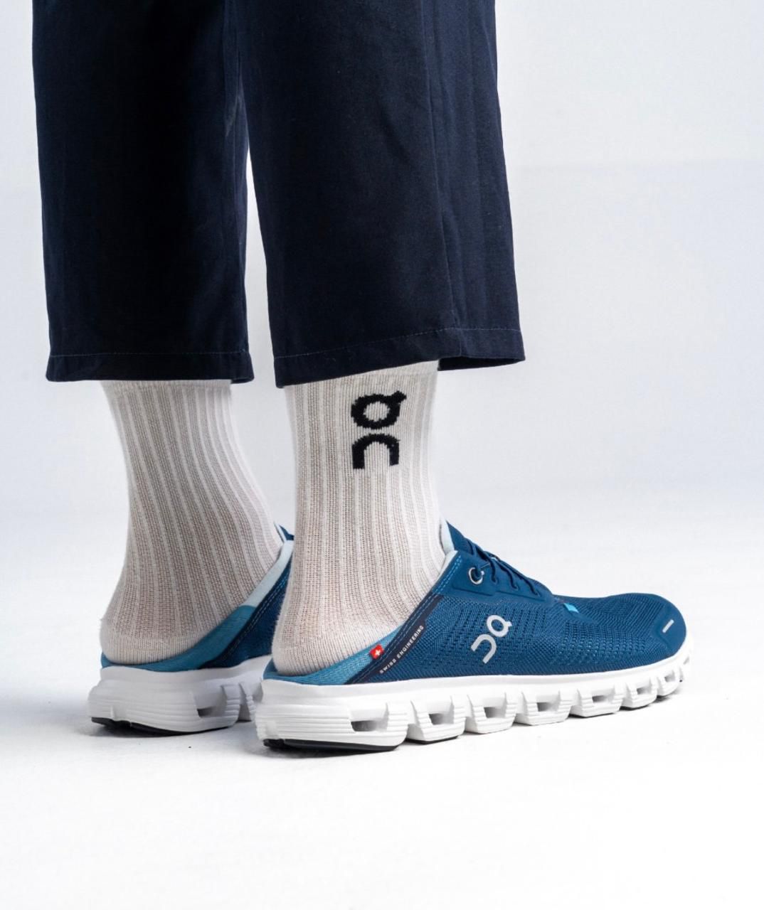 39f19d28-bff4-44ae-aeb5-fd0a965784c2 | UAE SPORT STORE Side view of blue On running sneakers with a white chunky sole, paired with beige ribbed socks and dark cropped pants.
