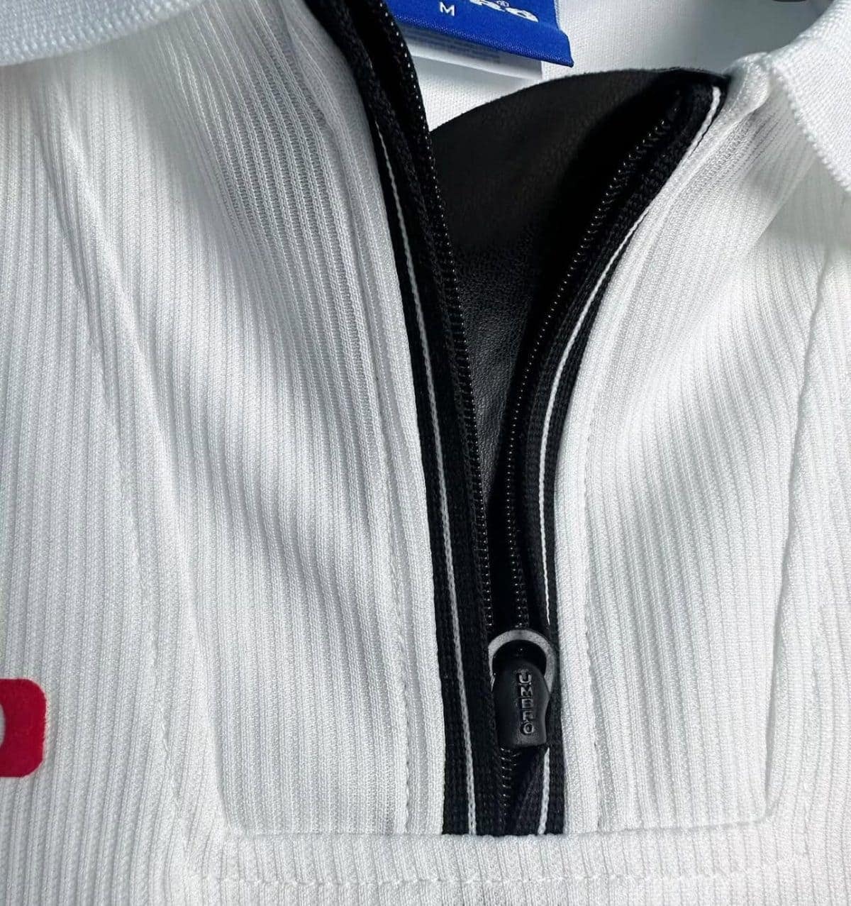 Close-up of a white ribbed zip-up sweater with a black zipper and zipper pull visible at the center