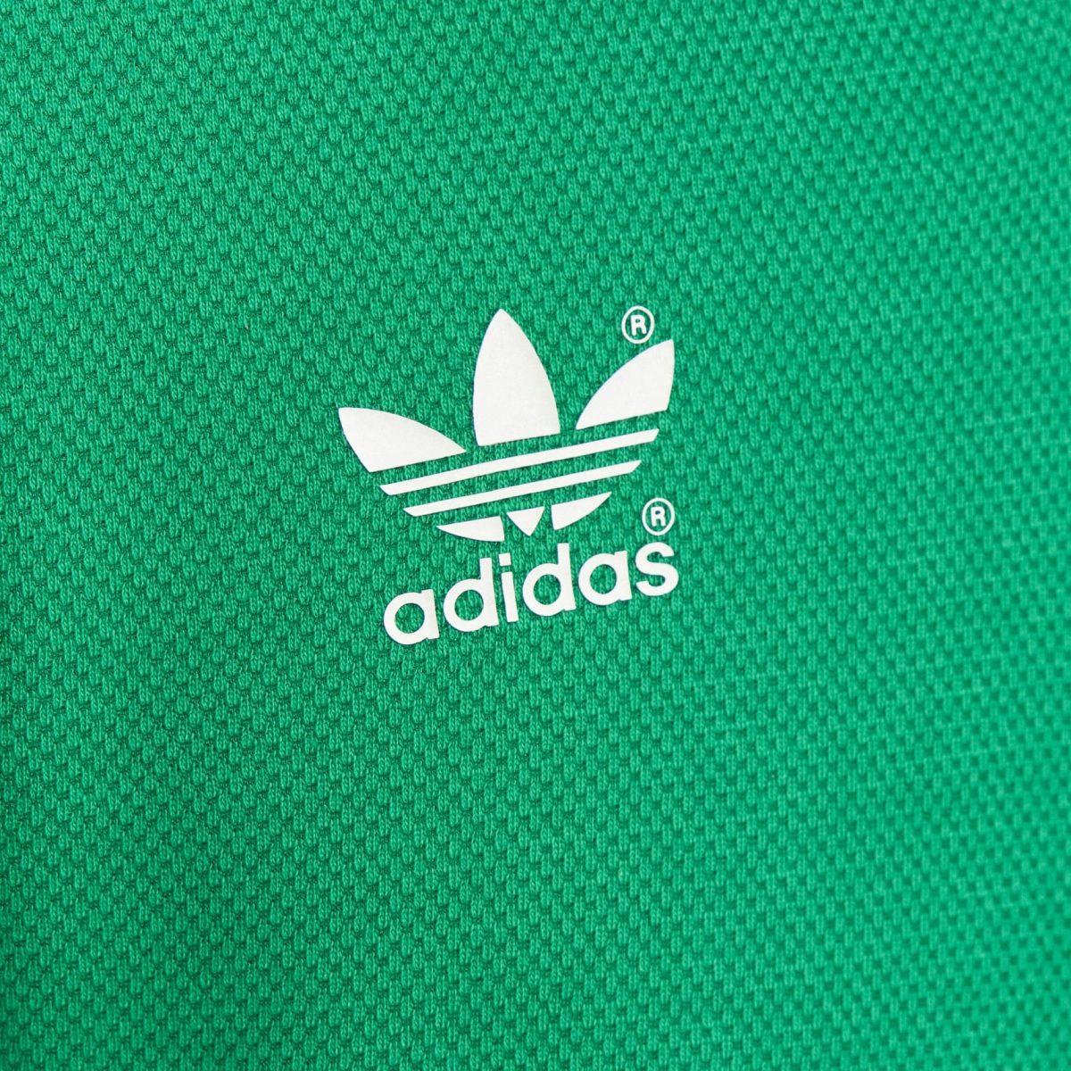 Close-up of a white Adidas trefoil logo on green textured fabric