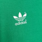 3CF38C3B-EF3D-4B88-8EEE-3028CDB1E704 | UAE SPORT STORE Close-up of a white Adidas trefoil logo on green textured fabric