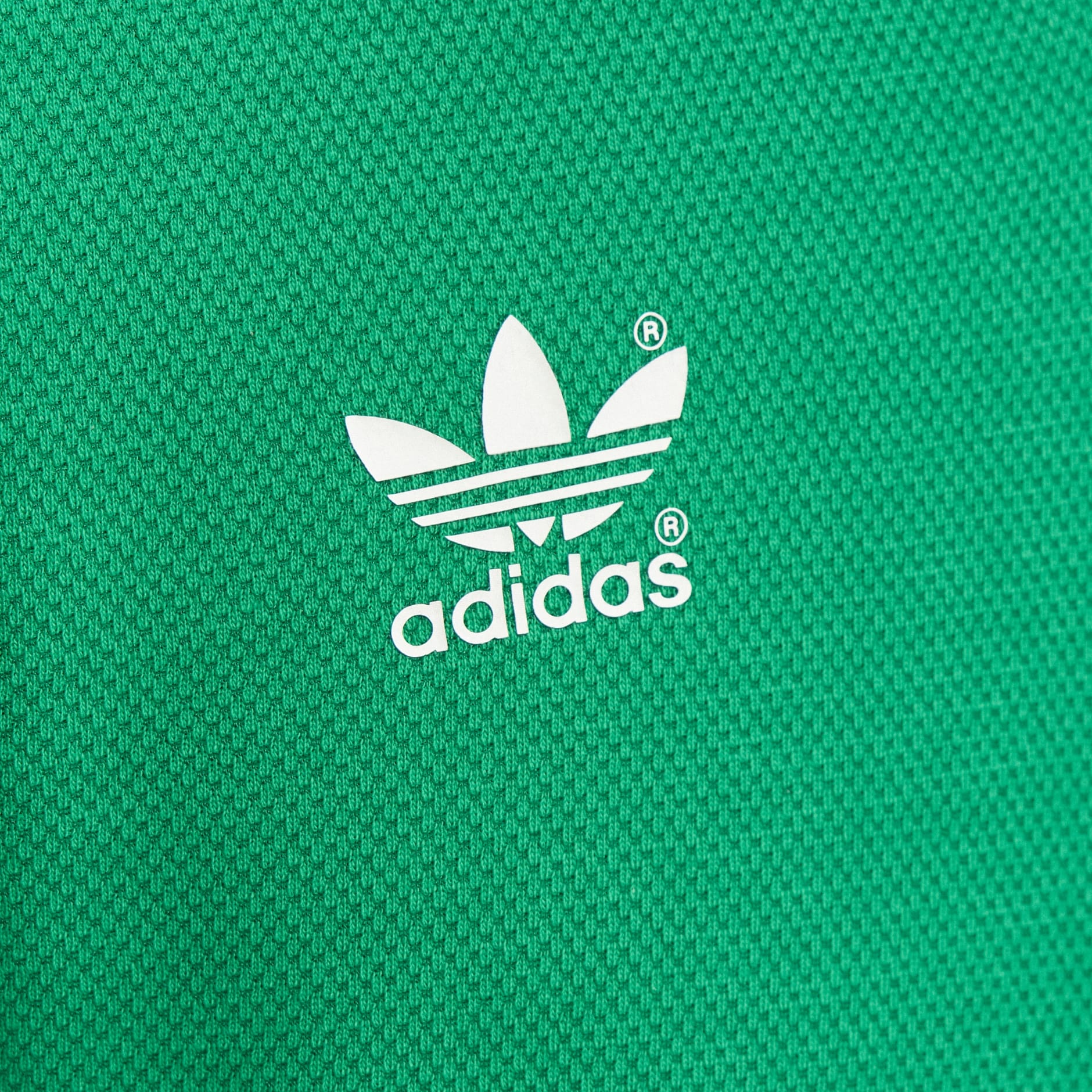 3CF38C3B-EF3D-4B88-8EEE-3028CDB1E704 | UAE SPORT STORE Close-up of a white Adidas trefoil logo on green textured fabric