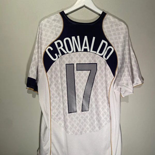 Back view of a white soccer jersey on a hanger, navy curved panel with gold trim reads 'CRONALDO' and the number 17
