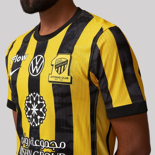 Close-up of a person wearing a yellow and black striped sports jersey with team crest and sponsor patches visible on the chest.