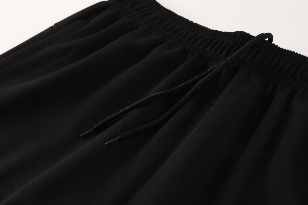 Close-up of black joggers showing an elastic waistband with drawstrings and metal tips (aglets).