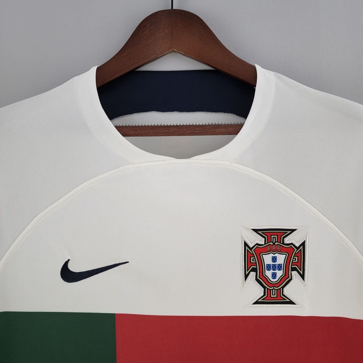 White sports jersey on a wooden hanger, showing a black Nike swoosh and the FPF Portugal crest.