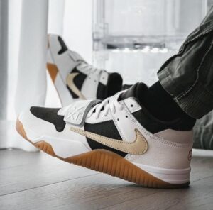 Close-up of white and black Nike sneakers with a beige swoosh and gum sole on a wooden floor.
