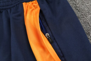 Close-up of navy athletic pants with a bright orange zippered side pocket on the seam for secure items.