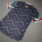 3a54eb63598e86a4 | UAE SPORT STORE Dark athletic jersey with a large zigzag pattern and multicolor striped sleeves laid flat on a gray surface.