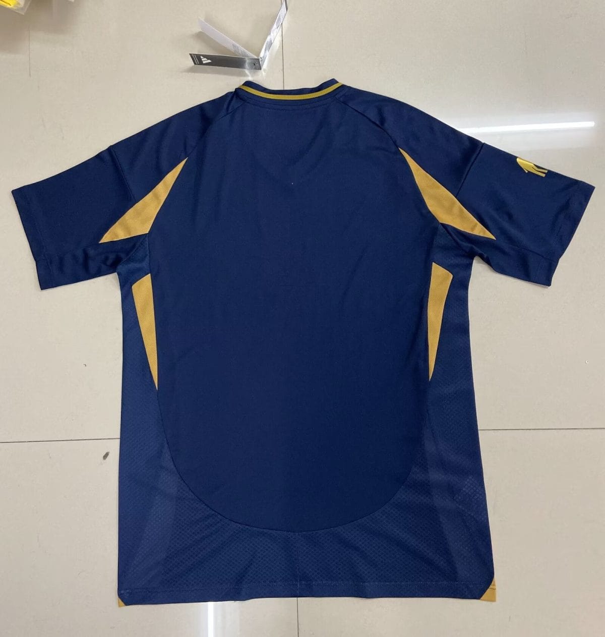 Back view of a blue athletic jersey with gold triangular panels along the sides and yellow trim at the collar.
