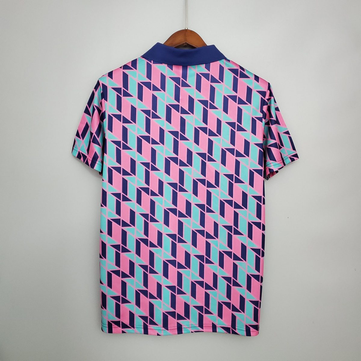 Back view of a short-sleeve shirt on a wooden hanger, featuring a pink, teal, and navy geometric triangle pattern and a dark blue collar.