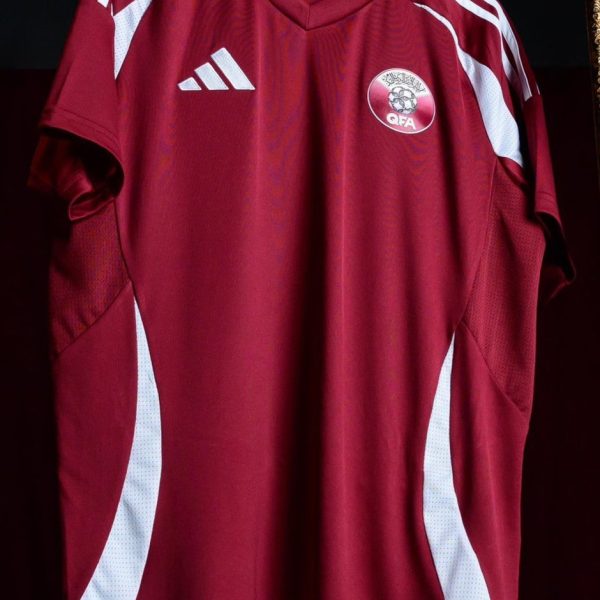 Maroon soccer jersey hanging on a rack with white Adidas stripes and a QFA crest on the chest area.0A sporty training jersey with maroon color and white side panels.