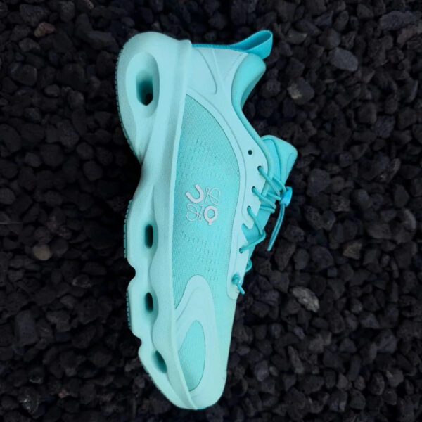 Turquoise running shoe on its side resting on dark gravel, showing the side and laces.
