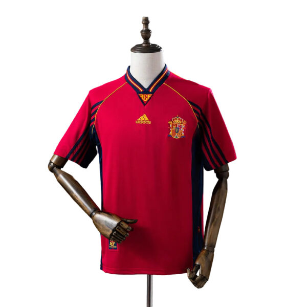 Spain national team red Adidas jersey on a mannequin, featuring the crest and yellow accents on the chest and sleeves.",