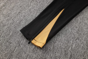 Black pant leg with an unzippered seam at the ankle, exposing a yellow inner lining.