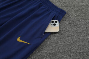 Navy blue Nike athletic shorts with a gold swoosh, a smartphone peeking out of a back/side pocket on a gray carpeted surface.