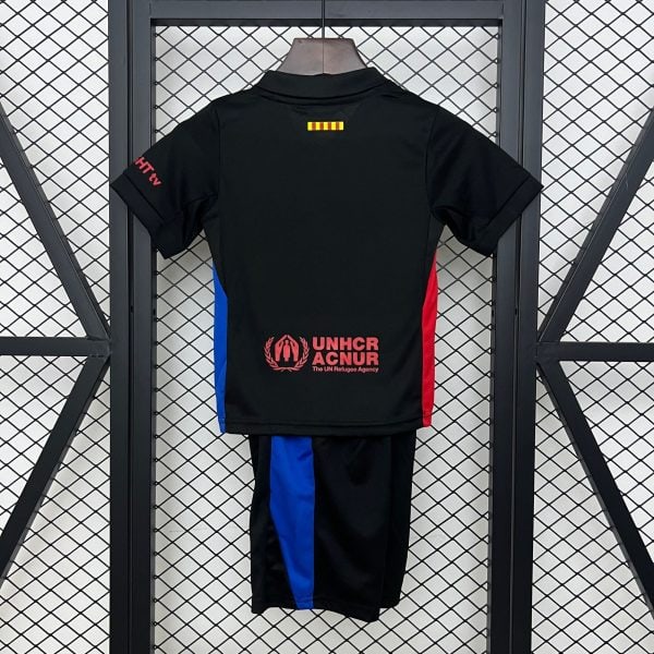Back view of a black athletic jersey hanging on a wooden hanger, with blue and red side panels and the UNHCR logo and text near the bottom main back area, against a metal grid backdrop with a small yellow-red striped patch at the upper center.