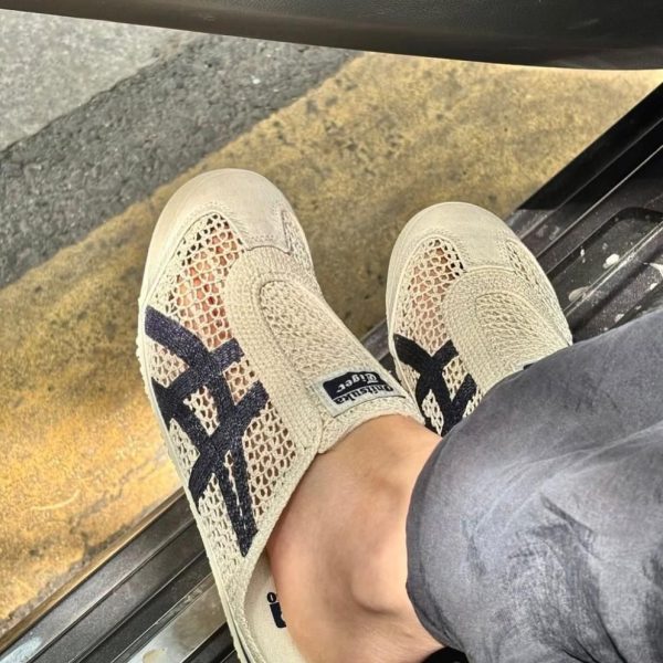 Beige mesh slip-on sneakers with dark cross stripes, a person resting one foot outside a car door.