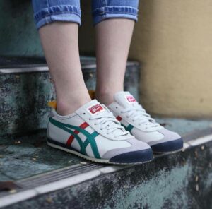 Person wearing white sneakers with teal and red side stripes standing on worn concrete steps outdoors.