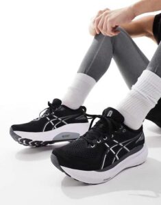3cbd6b88-b6c4-4692-9f1f-d1fd5149ac21 | UAE SPORT STORE Black athletic running shoes with white soles and laces, worn with gray leggings and white socks, resting on a white surface.