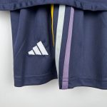 Close-up of a dark blue graduation gown with multi-colored tassels (yellow, light gray, lavender) hanging at the collar area and a white stitched logo on the fabric below.
