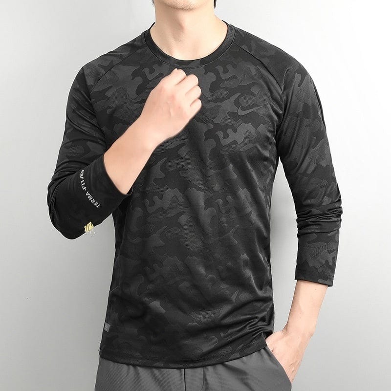 3d298672 | UAE SPORT STORE Male model wearing a black camouflage long-sleeve athletic shirt, standing against a light background with one hand near his chest.