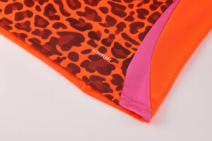 Close-up of bright orange athletic fabric with a pink side panel and pink leopard-print section, showing the AEROREADY logo.