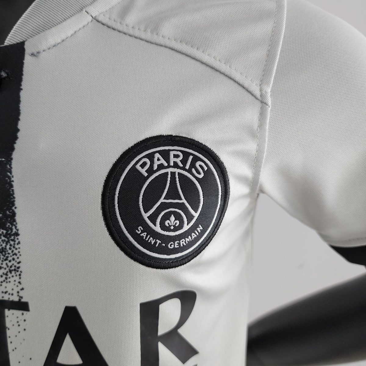 Close-up of light-gray fabric with a circular Paris Saint‑Germain patch stitched on.