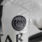 Close-up of light-gray fabric with a circular Paris Saint‑Germain patch stitched on.