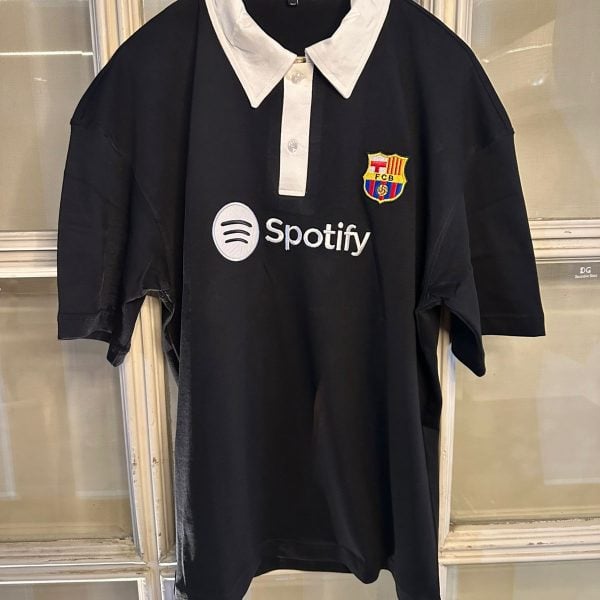 Black polo-style shirt on a hanger with a white collar, FC Barcelona crest, and Spotify logo on the chest.