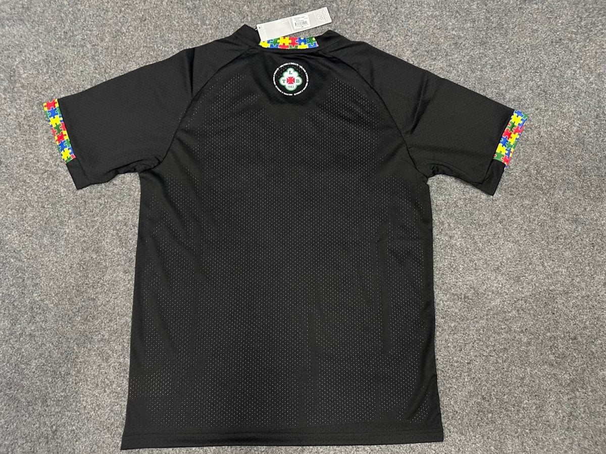 Black polo shirt with rainbow puzzle-piece trim on the collar and sleeve ends, and a circular emblem on the upper back.