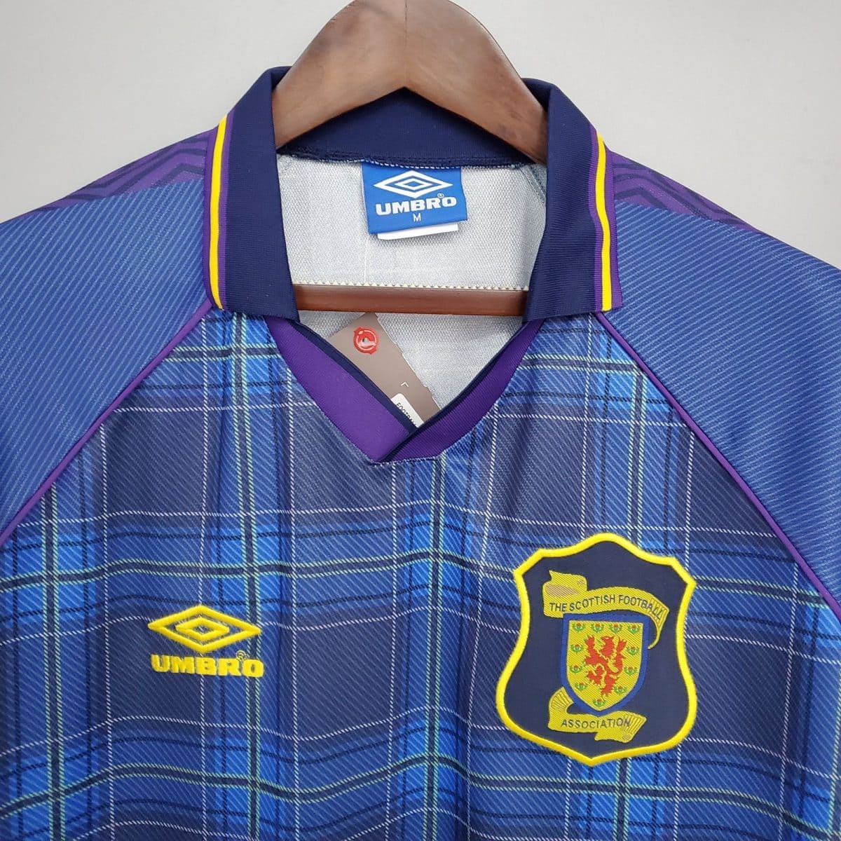Blue plaid soccer jersey on a hanger, showing Umbro tag and Scottish Football Association crest with purple and yellow trim.