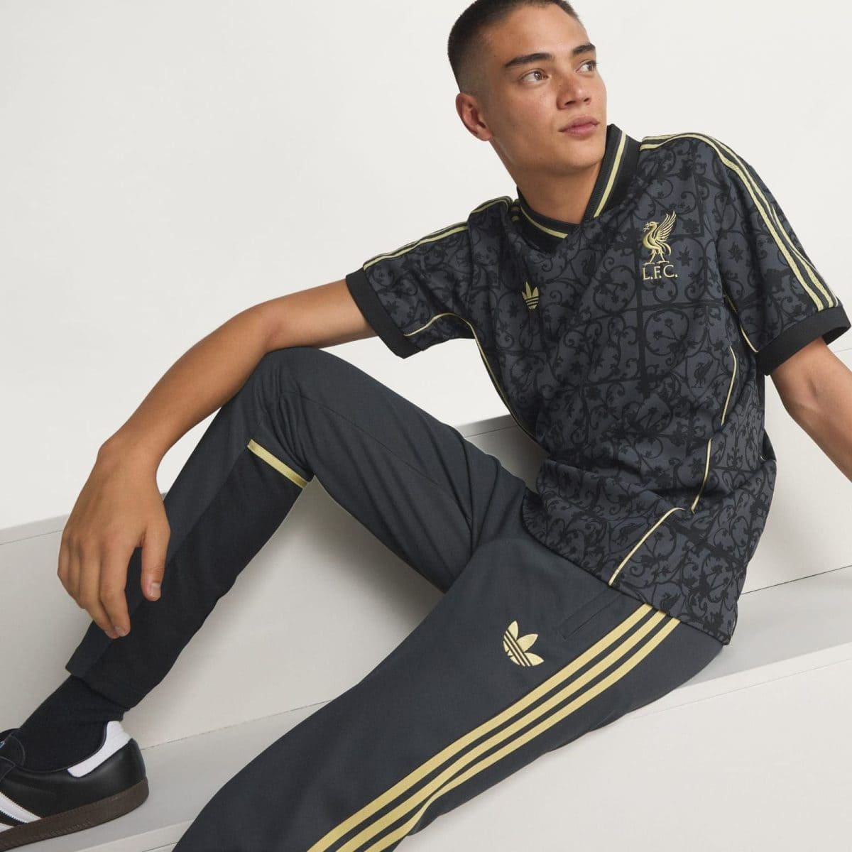 Young man in a black Liverpool FC training jersey with gold trim sits on white steps, looking to the right.