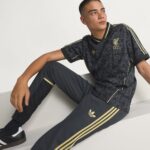 Young man in a black Liverpool FC training jersey with gold trim sits on white steps, looking to the right.