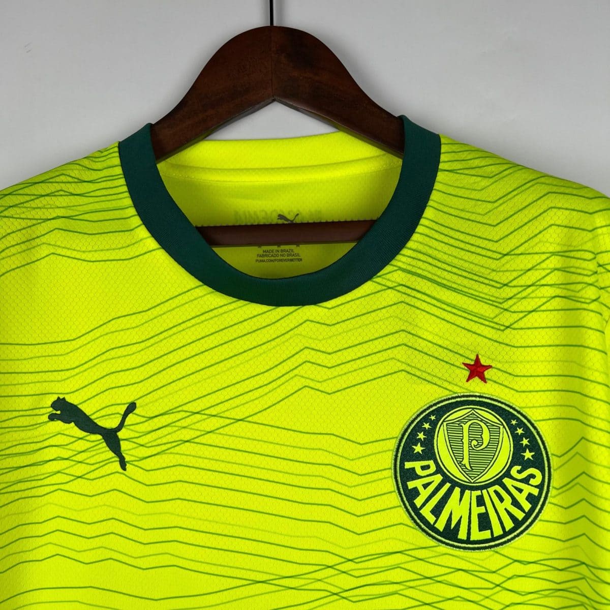 Neon yellow athletic jersey on a wooden hanger with a dark green collar, featuring a round crest at the lower right and a Puma logo nearby.