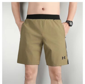 Man wearing tan athletic shorts with a black waistband; Under Armour logo on the left leg, hands in pockets, watch on left wrist.