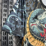 Short-sleeve shirt with a colorful dragon print draped over a metal rack with a chain-link background.
