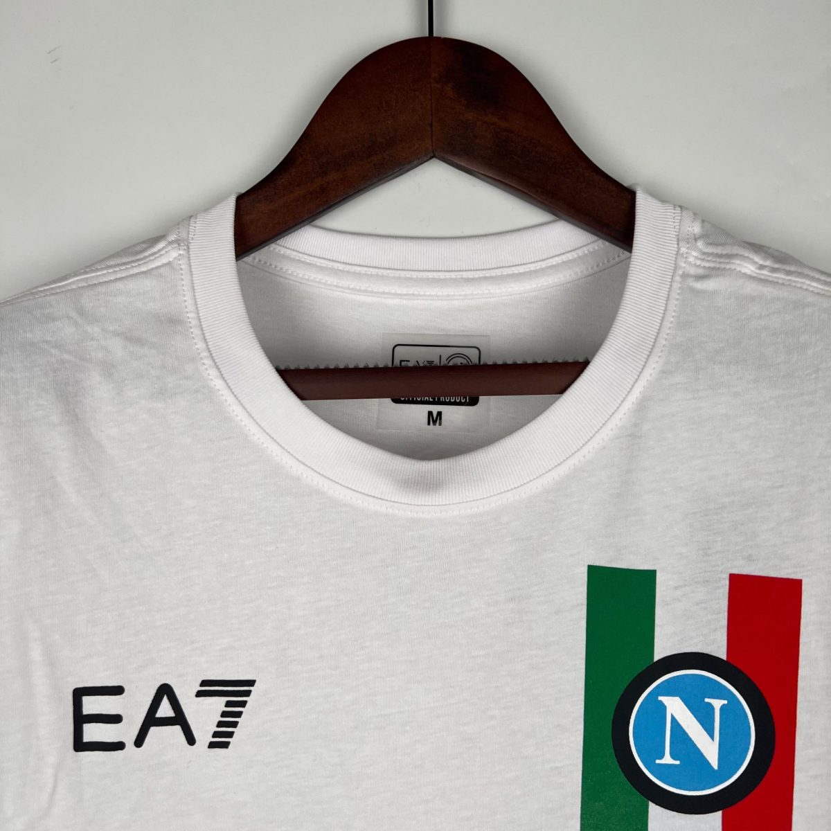 White crew-neck T-shirt on a dark wooden hanger against a light background, tag visible at the neckline edge.
