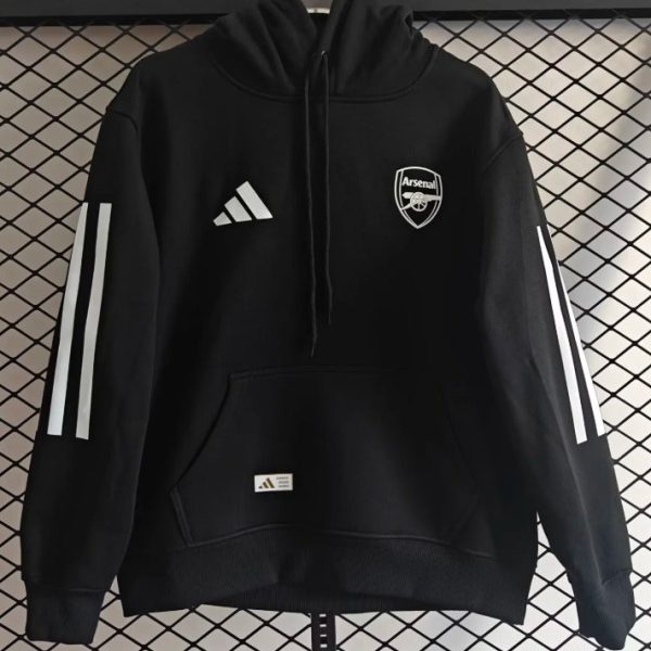 Black Arsenal hoodie with Adidas logo and crest, long sleeves with white stripes, front pocket, hanging against a chain-link background.