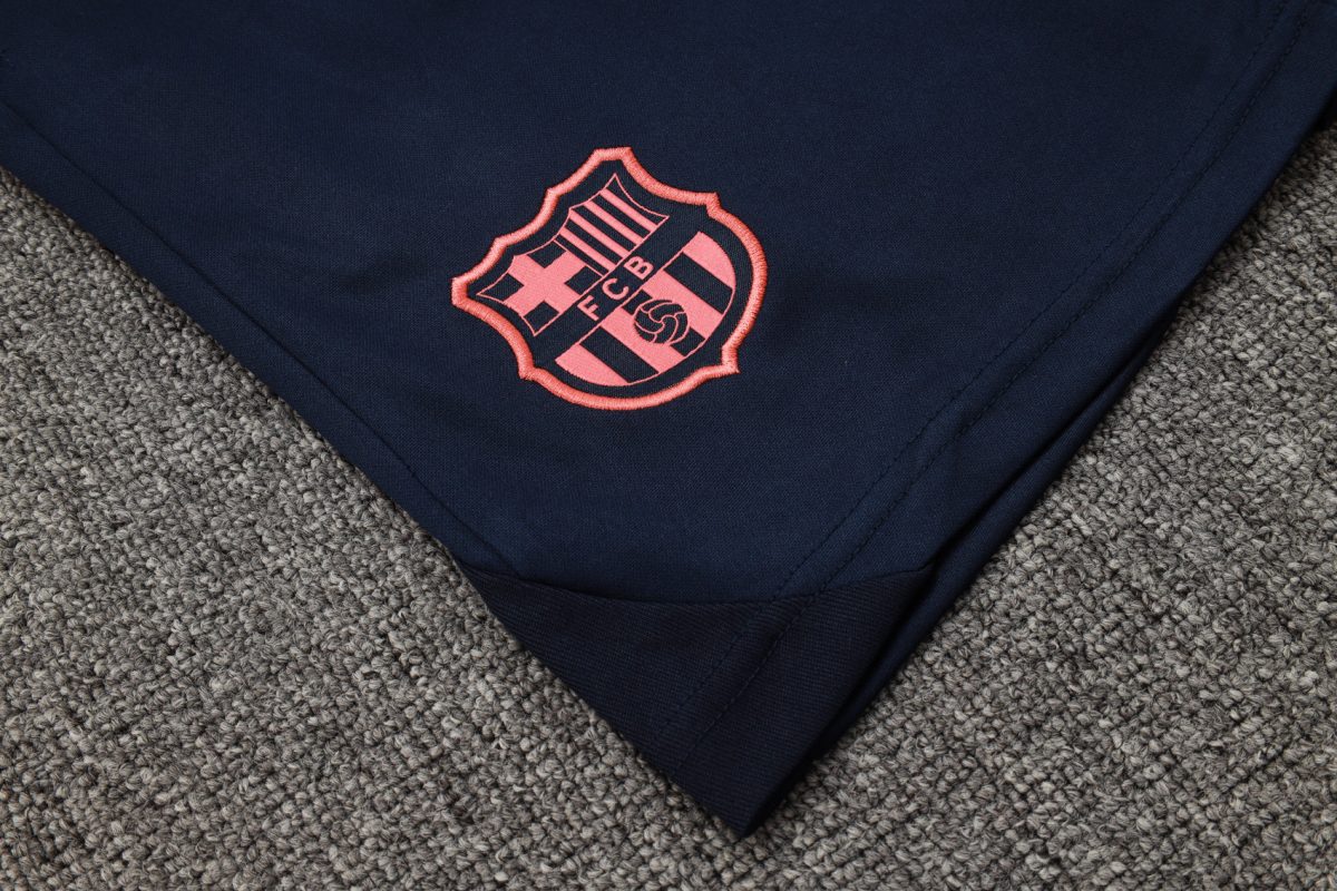 Navy fabric with a pink-embroidered FC Barcelona crest on the folded edge, resting on a gray carpeted surface.