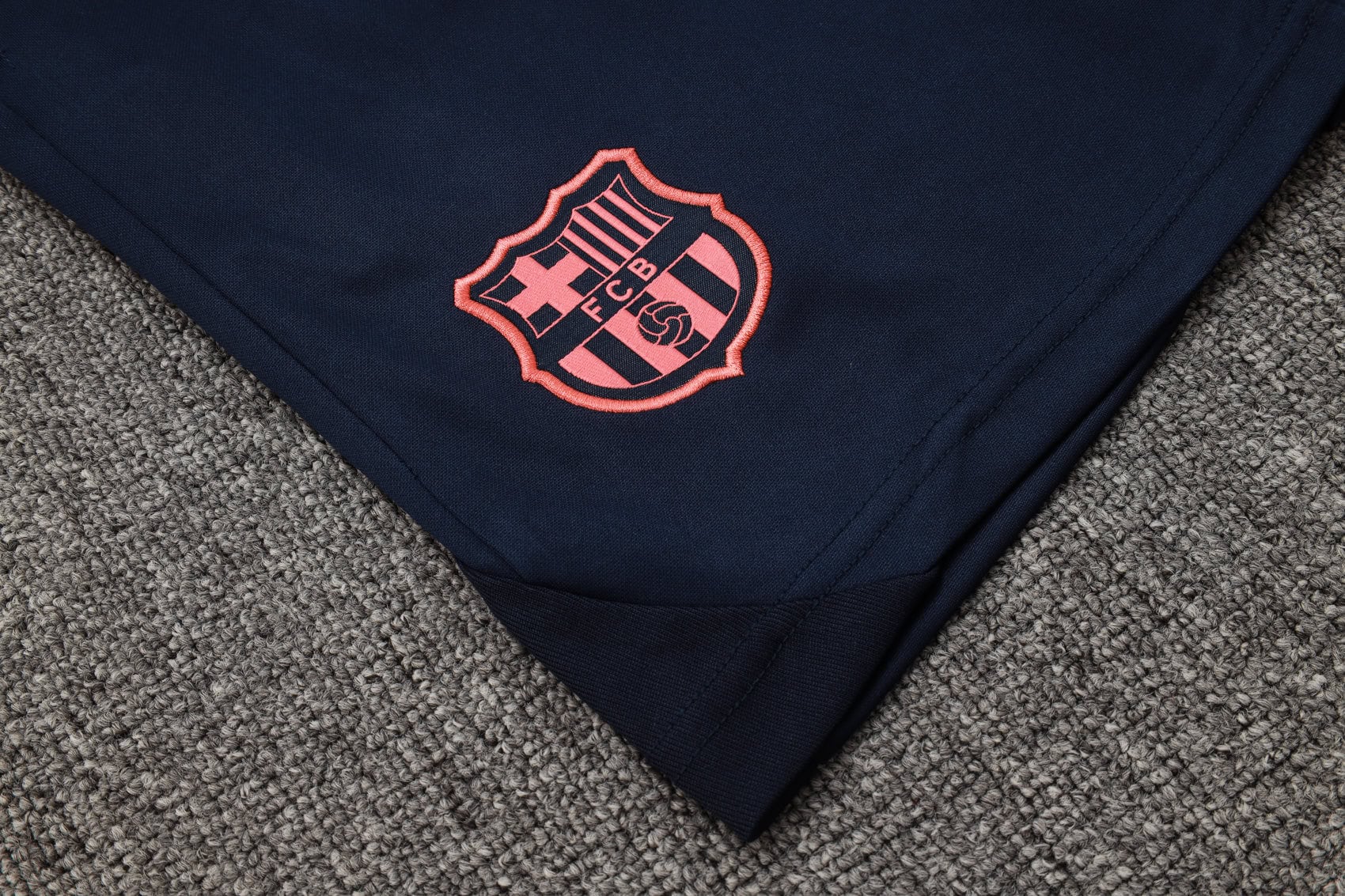 3f9cd96c | UAE SPORT STORE Navy fabric with a pink-embroidered FC Barcelona crest on the folded edge, resting on a gray carpeted surface.