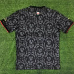 Back view of a black jersey with a repeating lion motif; near the collar note '1872 2024' and a small white shield with a red cross.
