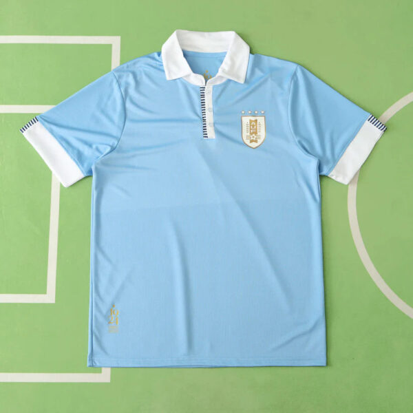 Light blue polo shirt with white collar and cuffs laid flat, crest on left chest on a green background.