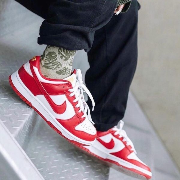 Close-up of red and white sneakers on a person stepping down a metal staircase, camo socks peeking out.