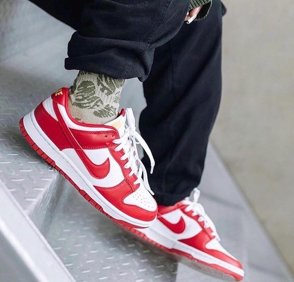 3ff3dcbe-acb6-4747-a685-4d932582fe3d_f0d46f01-0c5d-4295-8bcf-3b8eb04e32ec | UAE SPORT STORE Close-up of red and white sneakers on a person stepping down a metal staircase, camo socks peeking out.