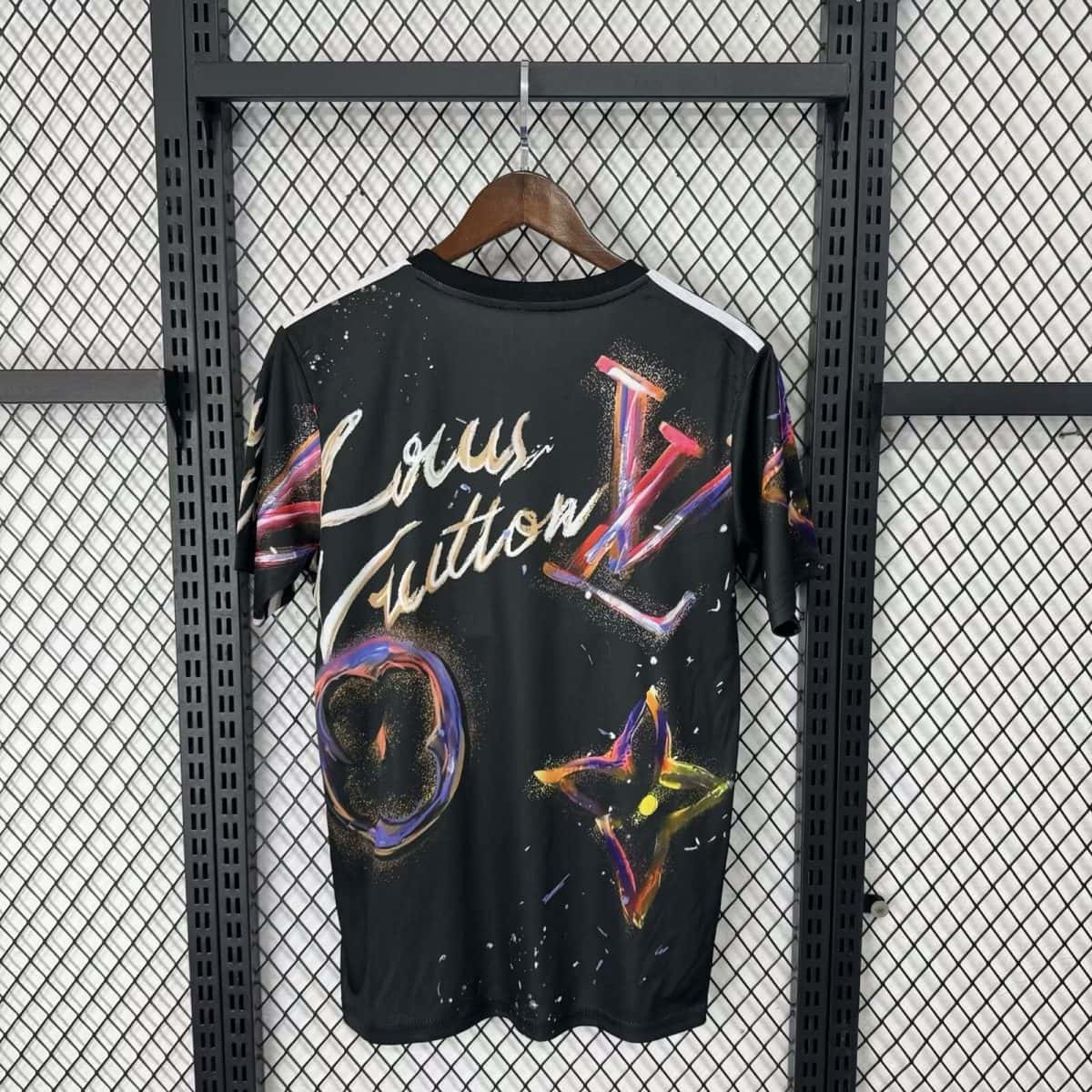 Black T-shirt on a wooden hanger with multicolored spray-paint design, hanging on a metal grid rack.