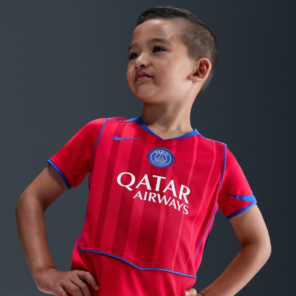 3q | UAE SPORT STORE Boy wearing a red PSG soccer jersey with Qatar Airways sponsor, standing with hands on hips against a dark background.