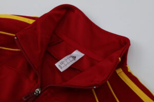 Close-up of a red Adidas track jacket with yellow piping and zipper, zipper pull visible.