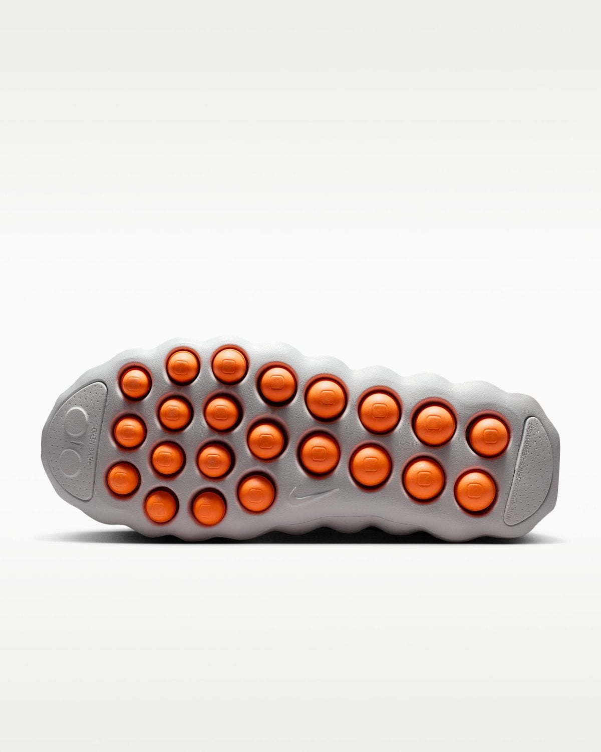 Bottom of a gray athletic shoe sole with bright orange circular grip pods arranged in rows, Nike branding visible at the edge.