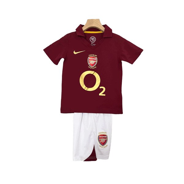 Maroon Arsenal football jersey with gold O2 logo on a hanger, paired with white shorts featuring the club crest.